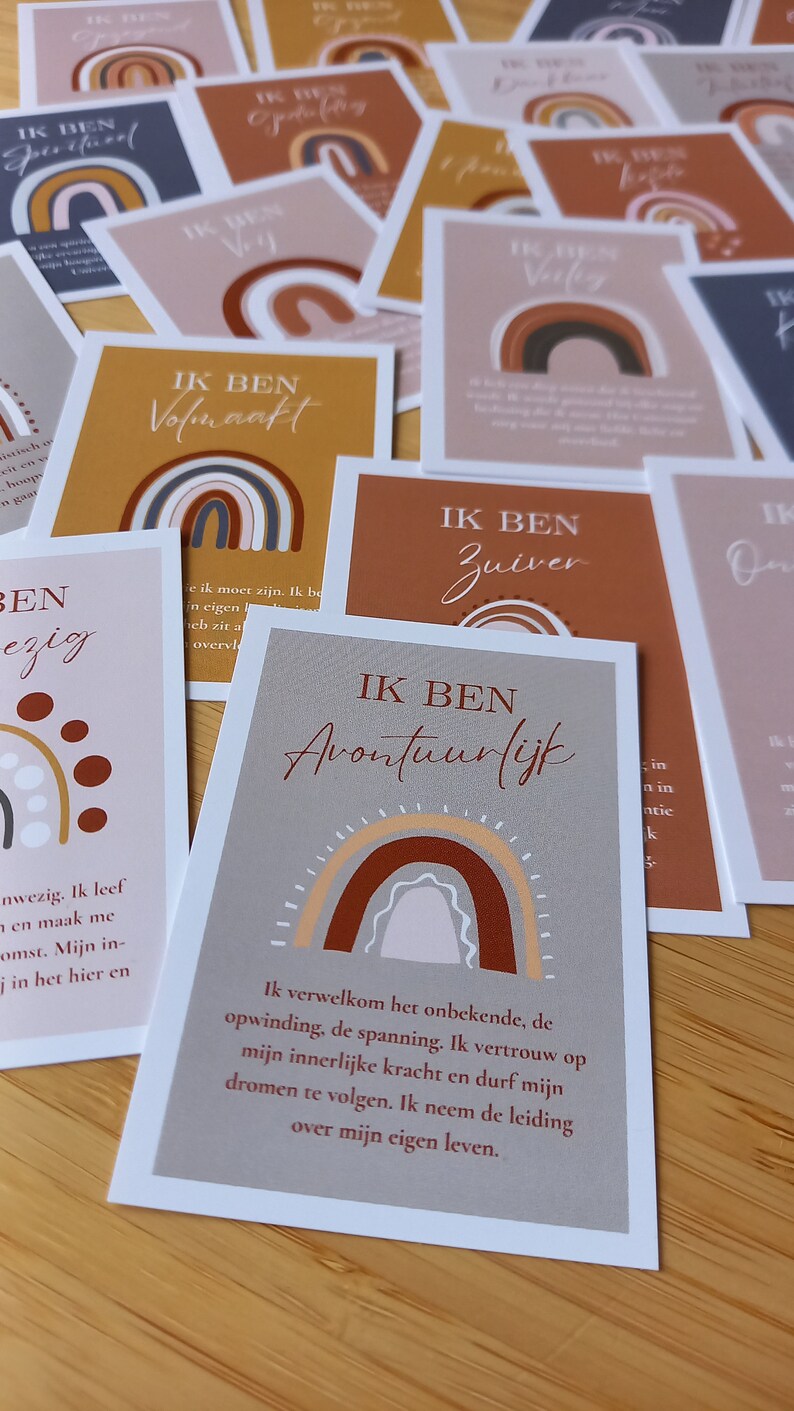 May include: A set of affirmation cards featuring a rainbow design and the text "IK BEN" followed by a positive affirmation in Dutch. The cards are printed on white cardstock with a brown background.