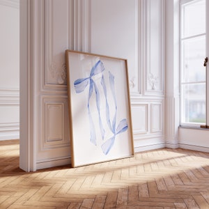May include: A framed watercolor painting of blue ribbons on a white background. The painting is leaning against a white wall with white molding.