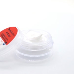 May include: A small, clear plastic jar with a white cream inside. The lid is red and has the text "Backofenfett HTS 600 Hochtemperaturfett für Teleskopauszüge" on it.