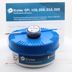 May include: A blue plastic container with a white label that reads "Krytox Performance Lubricants". A small, black jar with a white label that reads "GPL-20500 Contents: 5g Krytox" is sitting on top of the container. A small paintbrush is lying next to the jar.