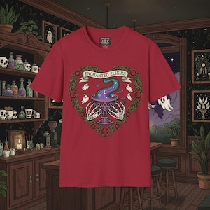 Puede incluir: Camiseta roja con un diseño en forma de corazón. El diseño presenta un caldero, manos de esqueleto, rosas y fantasmas, con el texto "ENCHANTED ELIXIRS". La camiseta es de cuello redondo.