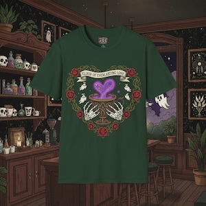 Puede incluir: Camiseta verde oscuro con un diseño en forma de corazón con el texto "Elixir of Everlasting Love". El diseño incluye una poción morada, manos de esqueleto, rosas y fantasmas. La camiseta tiene cuello redondo.