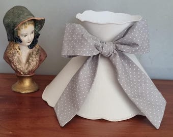 May include: A white lampshade with a scalloped edge and a gray polka dot bow. The lampshade has a conical shape and is paired with a vintage bust of a woman wearing a hat.