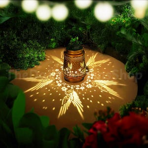 May include: A solar powered lantern with a metal design and a cut-out pattern of flowers and birds. The lantern casts a warm glow on the ground, creating a beautiful shadow pattern of flowers and birds.
