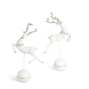 May include: Two white reindeer figurines with silver antlers and decorative collars. The reindeer are posed mid-leap, mounted on thin metal rods atop white spherical bases. A festive, decorative item.