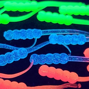 May include: Assortment of glow-in-the-dark fishing lures in blue, green, and red. The lures are made of soft plastic and have a segmented design.