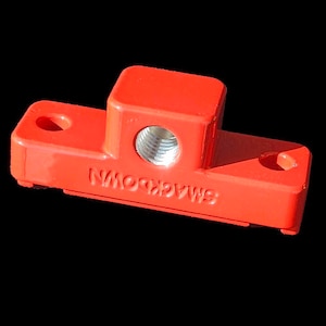 May include: A red metal electrical connector with the text "SMACKDOWN" printed on it. The connector has a threaded hole in the centre.
