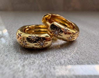 May include: A pair of gold hoop earrings with a starburst design and small clear stones.