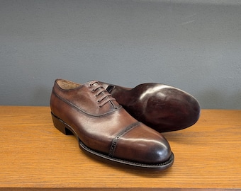 Sapatos sociais masculinos Oxford com biqueira perfurada e costura Goodyear, em couro de bezerro marrom com cadarço.