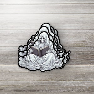 May include: A stack of ghost stickers with a ghost reading a book. The ghost is white with a black skull and is wearing a white robe. The book is black with a white spine.
