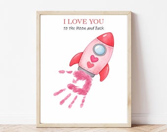 May include: A framed print featuring a pink rocket ship with red accents and a handprint trail. The text "I LOVE YOU to the Moon and Back" is written above the rocket. The artwork is in a wooden frame.
