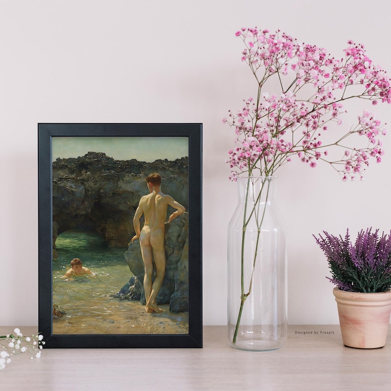 Op de afbeelding: Een ingelijste kunstdruk met een kustsc&egrave;ne met twee figuren. E&eacute;n staat op een rotsachtige oever, de ander zwemt in het water. Het kunstwerk staat in een zwart rechthoekig frame, met een vaas met roze bloemen en een potplant in de buurt.