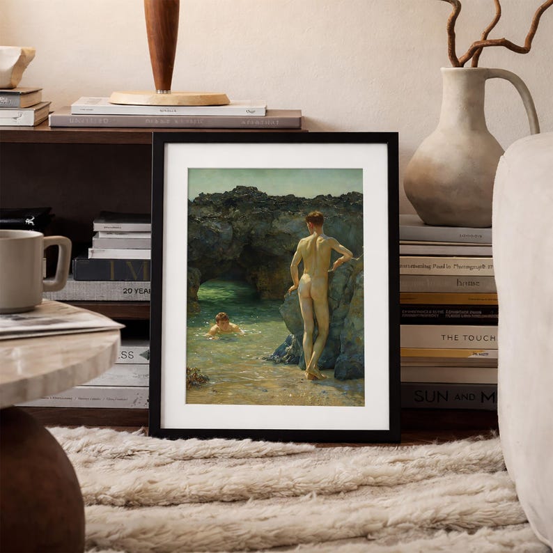 Op de afbeelding: Ingelijste kunstdruk met twee figuren in een kustlandschap. E&eacute;n figuur staat op een rotsachtige oever, terwijl een ander in het turquoise water zwemt. Het kunstwerk is ingelijst in een zwarte rand en rust op een beige tapijt.