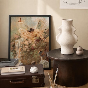 May include: A framed print featuring a classical painting of winged figures amidst flowers, a tall textured off-white ceramic vase, a small smooth beige vase, a white sculptural object, a brown vintage suitcase, and a book with a botanical cover.