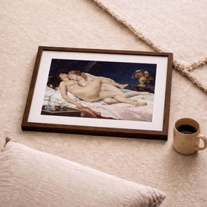 May include: A framed art print featuring a classical painting of two figures lying together on a bed with white linens. The dark blue background contrasts with the light skin tones of the figures. The frame is made of dark brown wood with a white mat.