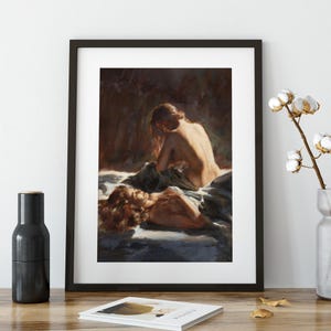May include: A framed art print featuring a painting of two figures. One figure is seated, and the other is lying down. The artwork has a warm color palette with shades of brown, beige, and blue. The painting is displayed in a black frame.