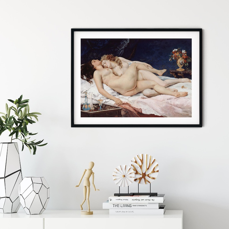 May include: A framed art print featuring a painting of two figures lying together on a bed with white linens. The scene includes a dark blue background, a small table with a vase of flowers, and a bedside table with a blue glass bottle and a goblet.