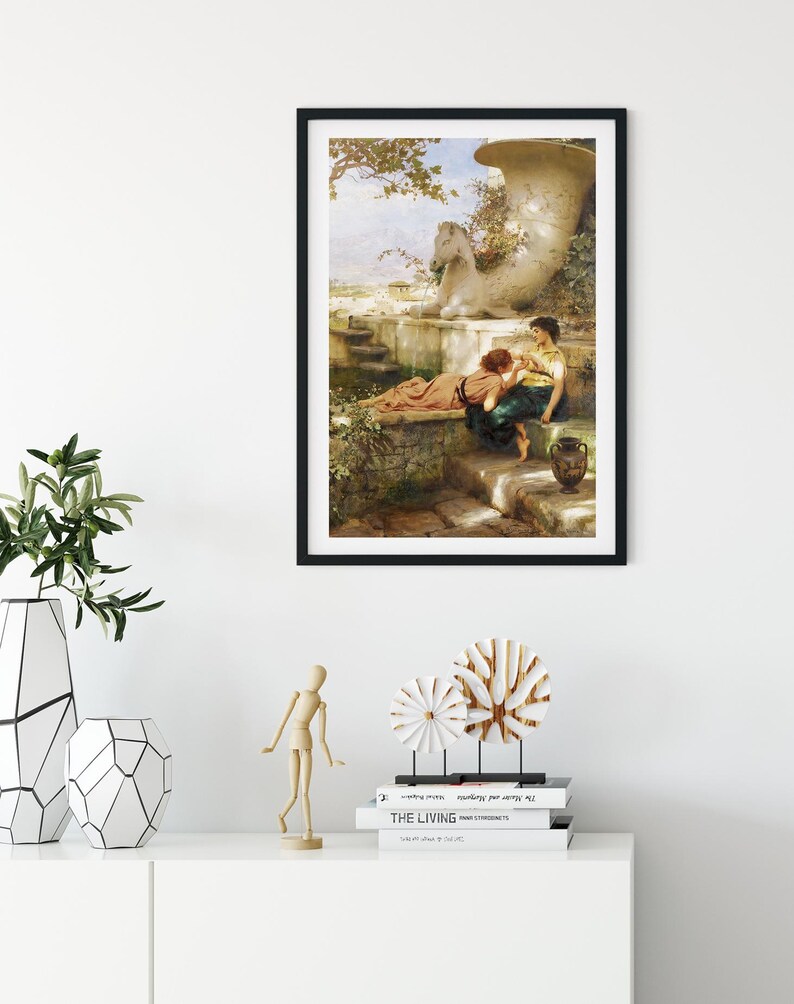 May include: Framed art print depicting a classical scene with figures near a large urn and a stone horse statue. The artwork is in a black frame, displayed above a white cabinet with decorative items, including vases and wooden sculptures.