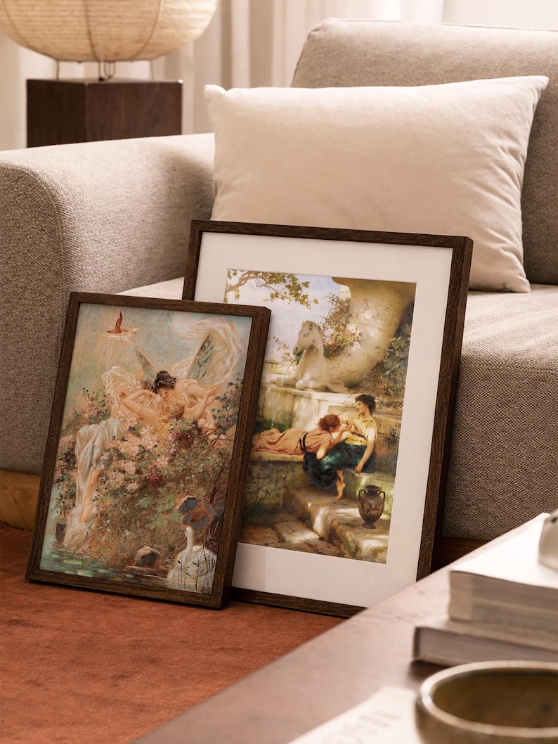 May include: Two rectangular framed art prints featuring classical paintings. The left print depicts winged figures amidst flowers and water. The right print shows two people sitting on stone steps near a white horse statue and a decorative urn.