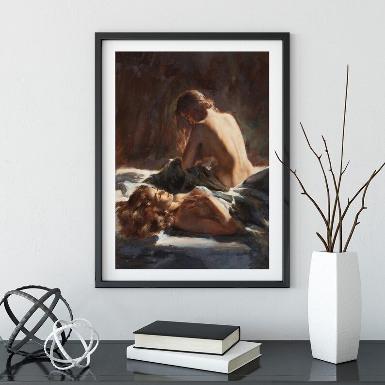 May include: Framed artwork featuring a classical painting of two figures. One figure is seated, the other reclining, both with reddish-brown hair. The painting has a warm color palette with soft lighting and is displayed in a black frame.