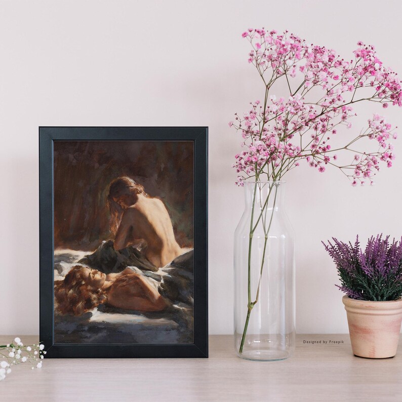 May include: A framed artwork featuring a classical painting of two figures. The painting depicts nude figures in a soft, warm color palette. A clear glass vase with pink flowers and a small potted plant are to the right of the frame.