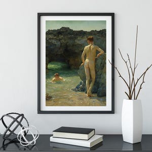 Op de afbeelding: Ingelijste kunstdruk van een klassiek schilderij met twee figuren op een rotsachtig strand. E&eacute;n figuur staat bij het water, terwijl een ander in de zee zwemt. Het kunstwerk is ingelijst in een zwarte rand.