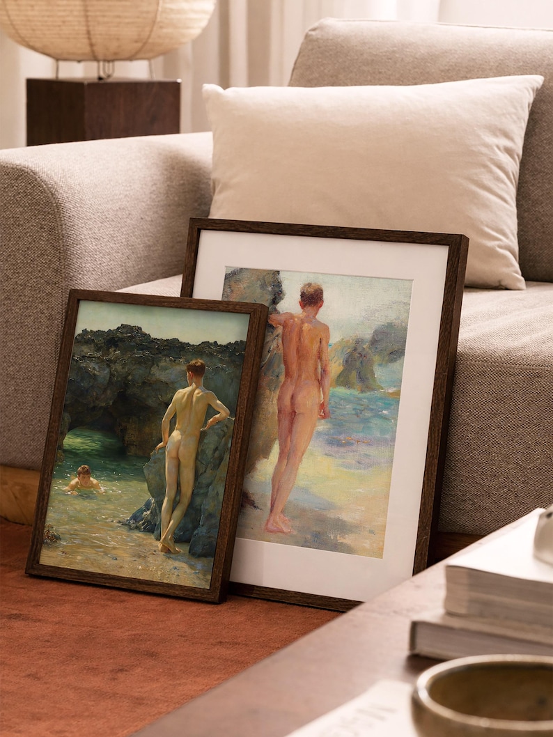 Op de afbeelding: Twee ingelijste kunstdrukken met klassieke schilderijen van naakte figuren aan zee. De prints hebben donkerbruine houten frames en worden tentoongesteld op een roodbruin tapijt voor een beige bank.