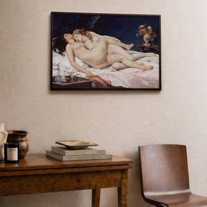May include: A framed horizontal wall art print depicting two figures reclining on a bed against a dark blue background. The scene includes a small table with a vase of flowers and a glass decanter. The figures are positioned on white and pink linens.