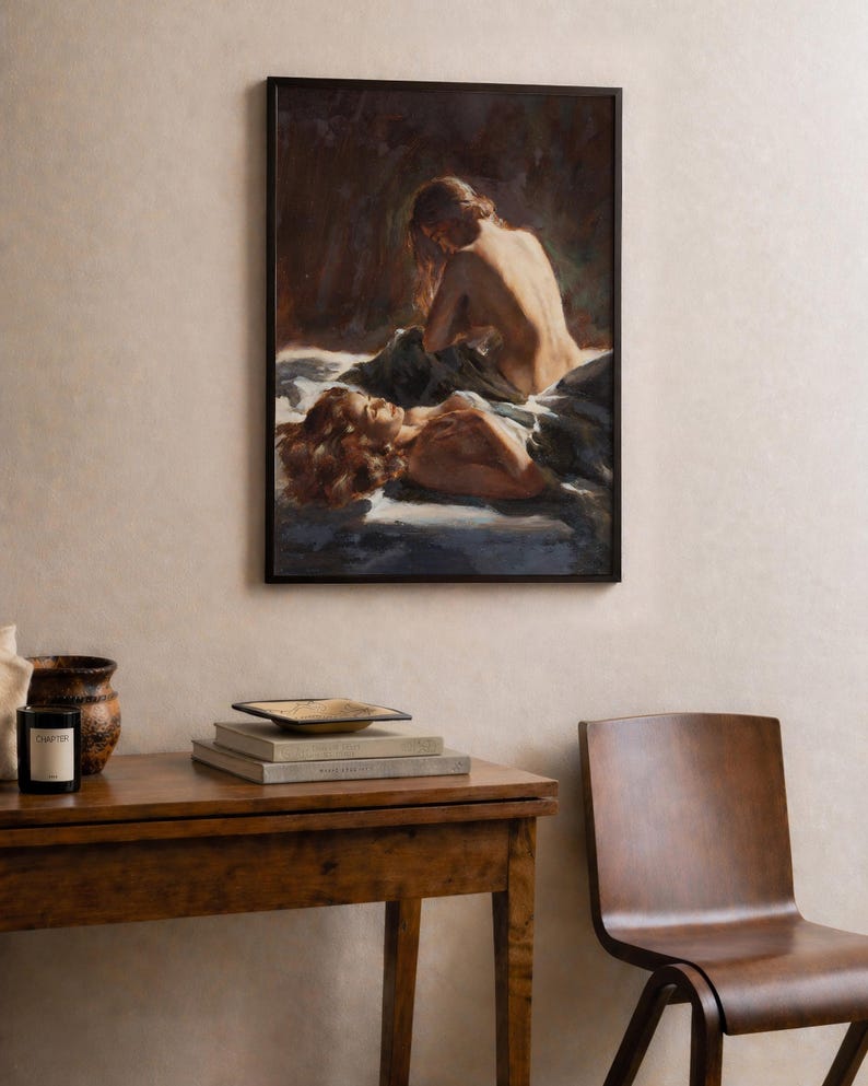 May include: A framed artwork depicts two figures in a bedroom setting. The painting features warm tones, with one figure seated and the other reclining. The artwork hangs above a wooden table with decorative items.
