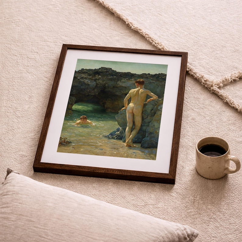 Op de afbeelding: Een ingelijste prent van een klassiek schilderij met twee naakte figuren bij een rotsachtige kustlijn. E&eacute;n figuur staat op de oever, de ander zwemt in het water. Een beige mok met donkere vloeistof staat in de buurt.