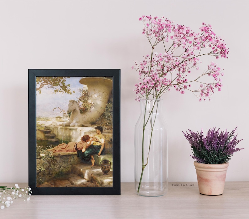 May include: A framed art print with a black frame depicts a classical scene with two figures near a fountain. A clear glass vase holds pink flowers, and a small potted lavender plant sits nearby. The scene is set on a light-colored wooden surface.