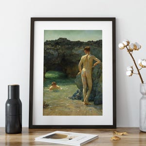Op de afbeelding: Ingelijste kunstdruk met twee figuren op een rotsachtig strand. E&eacute;n figuur staat op een rots, terwijl een ander in het water zwemt. Het kunstwerk gebruikt een gedempt kleurenpalet met een focus op natuurlijk licht en schaduwen.