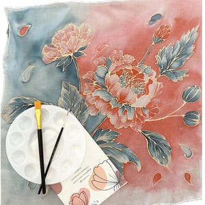May include: A silk scarf with a floral design in shades of blue, pink, and gold. The scarf is accompanied by a white paint palette with 12 wells and two paintbrushes. A small booklet with the text "explore painting techniques and create beautiful silk pieces" is also included.