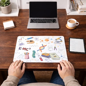 May include: A white desk mat with a colourful science-themed design featuring illustrations of a dinosaur, DNA, a microscope, and the equation E=MC². A laptop, tablet, and coffee cup are also on the wooden desk.