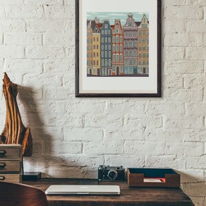 Pu&ograve; includere: Un'illustrazione incorniciata di una fila di edifici colorati con un cielo blu e nuvole bianche sullo sfondo. Gli edifici hanno finestre e porte bianche. L'illustrazione &egrave; su un muro di mattoni bianchi.