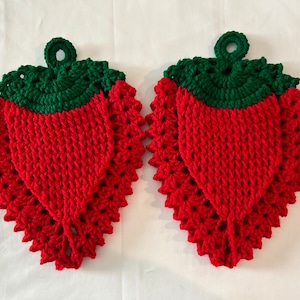 May include: Two handmade crochet strawberry-shaped potholders. The potholders are red with green tops and a hanging loop. The crochet stitch creates a textured surface, and the design is reminiscent of a fresh strawberry.