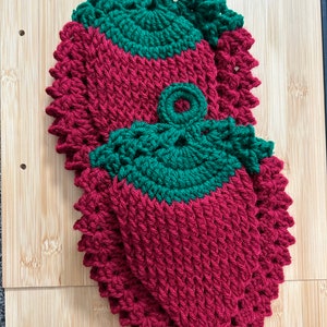 Peut inclure: Deux dessous de plat faits à la main en crochet en forme de fraises. Les dessous de plat sont principalement de couleur rouge foncé avec des dessus verts et une boucle pour les suspendre. Les dessous de plat sont sur une surface en bois brun clair.