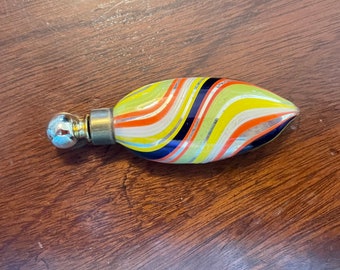 Könnte beinhalten: Eine kleine, bunte Glasflasche mit einem silbernen Stopfen. Die Flasche ist mit wirbelnden Streifen in Gelb, Orange, Weiß und Blau verziert.