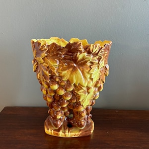May include: A ceramic vase with a brown and yellow glaze, shaped like a bunch of grapes with leaves.