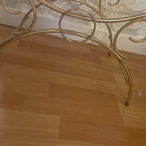 May include: A gold metal stand with a circular top and three legs. The stand is made of thin, decorative metal and has a delicate, ornate design.