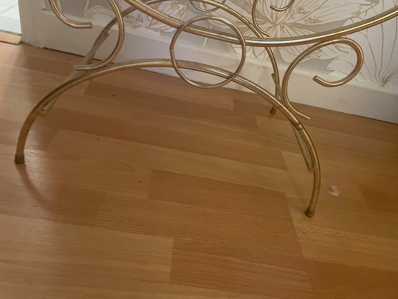May include: A gold metal stand with a circular top and three legs. The stand is made of thin, decorative metal and has a delicate, ornate design.