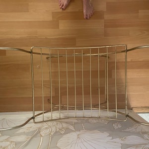 May include: Gold metal towel rack with a curved design and rounded ends. The rack has multiple bars for hanging towels.