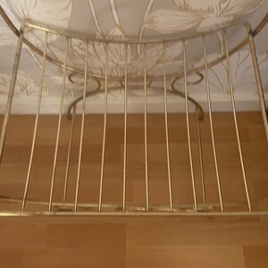 May include: A gold metal shelf with a curved top and a wire grid design. The shelf is empty.