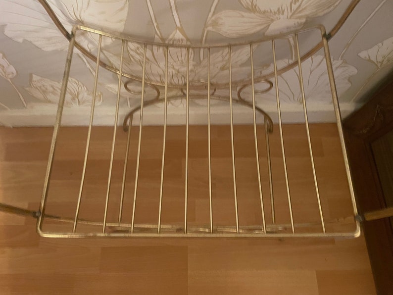 May include: A gold metal shelf with a curved top and a wire grid design. The shelf is empty.