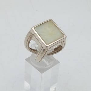 May include: A silver ring with a rectangular, light green stone. The ring has a thick band with a split design on each side of the stone. The stone is set in a square bezel.