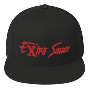 Może przedstawiać: Czarna czapka z daszkiem z płaskim daszkiem i haftem w kolorze czerwonym z napisem "Extra Sauce" w kolorze czerwonym.