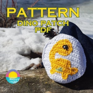 Peut inclure: Patron de crochet pour une applique de dinosaure jaune. Le patron s'appelle "Dino Patch" et est disponible en téléchargement PDF. Le patron est présenté sur un fond blanc avec un tissu denim bleu en arrière-plan.