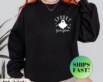 May include: Black sweatshirt with a white ghost graphic and the words "Spooky Season". The design includes bats. The sweatshirt is a dark color and suitable for Halloween or fall.
