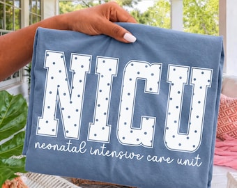 May include: A blue t-shirt featuring the white text NICU in a large block font with a polka dot pattern. Below the large letters, the words neonatal intensive care unit are printed in a white cursive script. The fabric is a solid blue color.