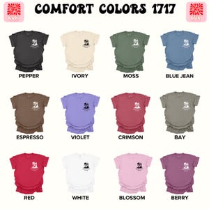 Pode incluir: Uma cole&ccedil;&atilde;o de camisetas Comfort Colors 1717 em v&aacute;rias cores, incluindo pimenta, marfim, musgo, azul jeans, expresso, violeta, carmesim, ba&iacute;a, vermelho, branco, flor e berry. Cada camisa apresenta um pequeno gr&aacute;fico e texto. O logotipo da marca est&aacute; nos cantos superiores.